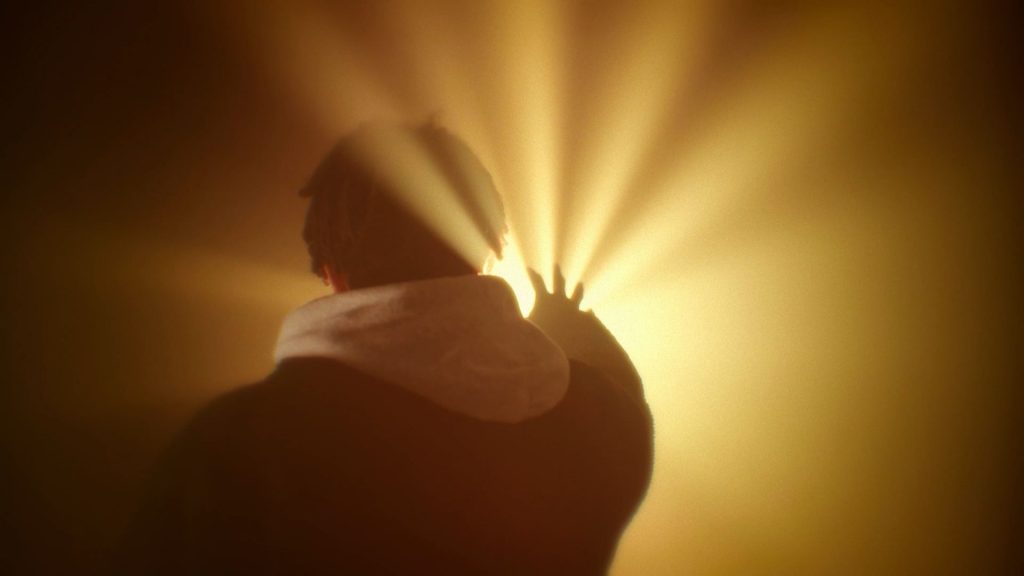 Baboune artiste rap bordelais en contre jour tend la main vers une lumière doré